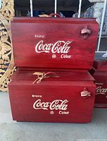 Two stacked red wooden Coca Cola coolers showing front logos and bottle openers.