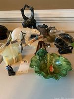 Photo displaying the collection of animal figurines including giraffes, polar bear, black cat, frog on green leaf dish, birds and ducks figurines on table.