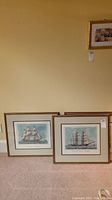 Two frames leaning against a wall on carpet with visible tags, showing ship prints.