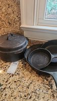 Photo showing Griswold #8 Dutch oven with lid alongside three Wagner Ware frying pans of different sizes on a countertop.