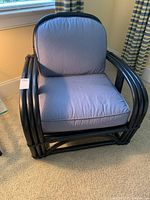 Front view of black painted rattan chair with blue cushions placed on carpeted floor under window.