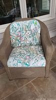 Front view of Lloyd Flanders wicker lounge chair with floral cushions on a tiled porch floor.