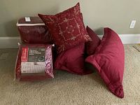 Photo showing the packed Sunbeam heated mattress pad, red comforter and decorative pillows including a floral embroidered pillow and others