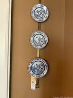 Three blue and white decorative plates displayed vertically on brass wall hanger