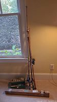 Photo showing four fishing rods standing upright, including the vintage boxed Sakura rod, and a green tackle box on the floor.