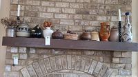 Full view of pottery collection, basket, and candle holders displayed on wooden mantel against brick wall.