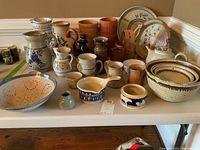 Full view of entire collection showing pitchers, bowls, mugs, wine chillers, teapot, and plates arranged on a table against a wall.