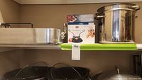 Shelf showing Oneida large roasting pan with handles, Tools of the Trade large steamer pot, and boxed fondue pot