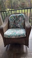 Front view of the Lloyd Flanders woven rocking chair with floral patterned cushions on porch.