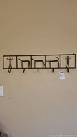 Full view of wrought iron wall rack with hooks and decorative figures mounted on wall.