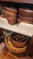 Three wooden salad and mixing bowls stacked on a shelf and wooden trivets resting in a larger wooden bowl beneath.