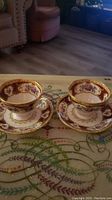 Photo of two Royal Albert teacups with matching saucers on a decorated glass table. Shows overall design and condition.