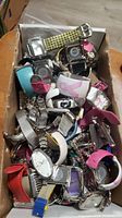 A cardboard box filled with assorted watch faces and watch bands of various colors and designs.