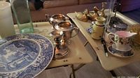 Showing ceramic blue and white plate, silver candle holders, porcelain teacup with floral design and small pitcher on table.