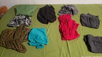 Various large women's tops and shorts laid out on a bed including green, animal print, black, brown, turquoise, red, and grey items.