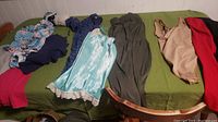 Photo showing a selection of various large size women's clothing including dresses, tops, and undergarments spread on a green bedspread.