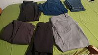 Folded women's pants and jeans in dark colors with one light grey pair laid out on a green surface.