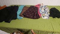 Seven different women's clothing items including a black blazer, turquoise blouse, brown skirt, burgundy plaid skirt, coral pink blouse, multicolored patterned blouse, and a black head wrap.