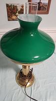 Photo of vintage lamp showing the green glass shade and brass base on a white surface, capturing the full lamp height and shape
