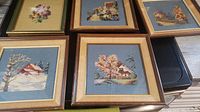 Top view of five framed needlepoint artworks displaying house and floral scenes, all with wood frames and blue background fabric