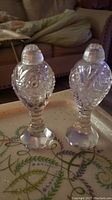 Pair of vintage clear glass perfume bottles on a patterned surface, showing overall shape and design.