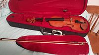 Full violin, bow laid inside the case with red interior lining showing the violin and bow condition