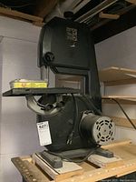 Side view of the band saw showing the motor, base, and work table on wooden blocks.