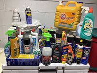 Photo showing the full lot of cleaning and car care supplies displayed on a table against a concrete wall, showcasing multiple branded bottles, sprays, and containers.