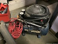 Side view of Mastercraft air compressor showing upper motor housing, pressure gauges, red coiled air hose and blue cylindrical tank.