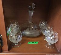 Full view of the etched glass decanter with stopper and five matching cordial glasses, all featuring a nautical sailing ship design etched in frosted glass.