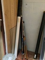 Fishing rods and tubes standing in corner on wood floor against white block wall and wood paneling