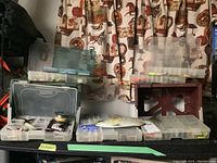 Three clear plastic tackle boxes open on metal shelf showing assorted lures and accessories.