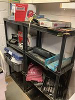 Wide view of black plastic three-tier shelving unit holding various tools including Jobmate jigsaw box, rotary accessory set, tool cases, and hardware items.