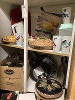 Overview of kitchen cabinet shelf showing ceramic pie dishes, glasses with bird designs, white pitcher, and packaged corn meal mix.