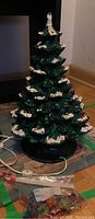 Green ceramic Christmas tree with white snow tips shown standing on floor with electrical cord visible.