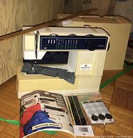 Front and side view of Husqvarna Optima 620 sewing machine with fabric under needle, case in background, and accessories including manual and extras in front.