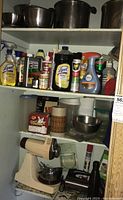 Shelf showing multiple stainless steel pots on top shelf, cleaning products and kitchen items on middle shelf, and stand mixer and hand mixer on bottom shelf