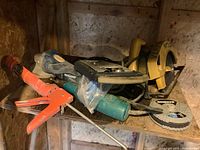 Photo of miscellaneous tools on wooden shelf, showing an orange caulking gun, a Mastercraft angle grinder, and yellow circular saw partially visible.