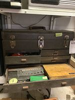 Closed metal tool box with drawers open to show contents including metal plates and hardware