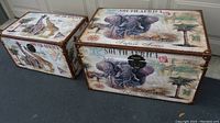 Both safari-themed canvas trunks side by side, showing giraffe and elephant designs, leather trim, and condition.