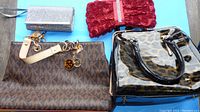 Four purses shown together: Michael Kors large tote with logo charms, red rosette clutch with rhinestone strip, silver glitter clutch, leopard print glossy handbag