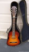 Full view of acoustic guitar in open hard case showing sunburst finish and six strings