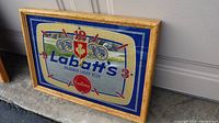 Photo of vintage Labatt's bar sign resting angled on the ground, showing front design and wooden frame.