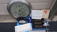 Photo of large round wall clock, small black oval clock, silver rose in box, multiple inspirational and decorative signs, and masquerade mask spread out on the ground.