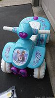 Front view of the light blue Disney Frozen 6V quad ride-on with purple heart accents and character decals.