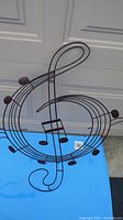 Full view of black metal musical note wall décor in the shape of a treble clef on blue surface.