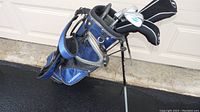Full view of blue and black golf bag with clubs, showing stand legs and compartments.