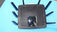 Top view of black Linksys EA9500 router with eight antennas and central glossy panel with Linksys branding.