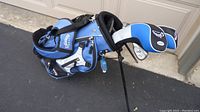 Full view of the blue, white, and black Callaway golf bag with stand and several zippered compartments, including the clubs inside with headcovers on driver and fairway woods.