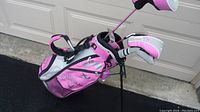 Photo showing pink and gray Callaway golf bag with stand and multiple golf clubs with headcovers inside.